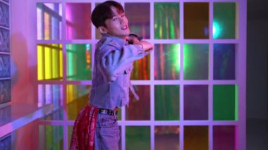 Kameraya bakarken kollarını esneten seksi kıyafetli Asyalı dansçı. Profesyonel sanatçı gece kulübünde renkli neon ışıkları canlı bir şekilde dururken serbest stil dansı yapıyor. Mutluluk.