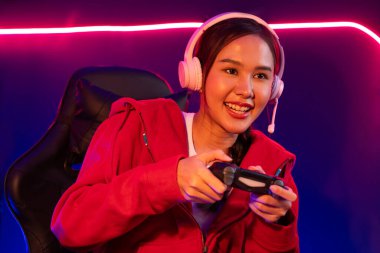 Oyun çubuğu ile gülümseyen Asyalı güzel kız flamasının sunucu kanalı kulaklık yapıştırıcısı takarak online izleyici medyasıyla konuşuyor. Esport yetenekli takım oyuncuları neon odada. Taktik.