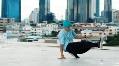 Beyaz tenli dansçı çocuk çatıda sokak dansı yapıyor şehir siteleriyle ya da şehirlerle. Genç adamın sokak dansı yaparken dondurucu poz vermesi. Açık hava sporu 2024. Hiphop.