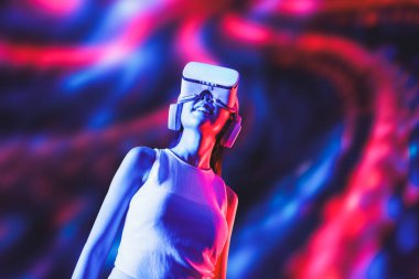 Zeki bir kadın, metaevreni birbirine bağlayan VR kulaklık takan neon ışıklarla çevrili duruyor. Gelecekteki siber uzay topluluğu teknolojisi. Uzaklara bakan zarif bir kadın ve tatmin edici bir şekilde gülümsüyor. Halüsinasyon.