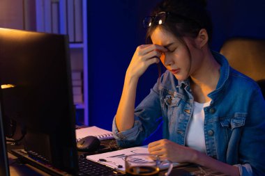 Stresli, genç, güzel Asyalı yaratıcı proje yaratıcısı sosyal medyayı araştırmak için bilgisayara bakıyor ve geceleri daha çok neon modern ofisin planlama kanalı stratejisine ulaşılıyor. Taktik.