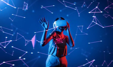 Beyaz VR kulaklık takan ve metaevreni birleştiren kolsuz tişört giyen, gelecekteki siber uzay topluluğu teknolojisi olan bir kadın siber punk neon ışığı altında el ve vücut hareketleriyle dans etmekten zevk alıyor. Halüsinasyon.