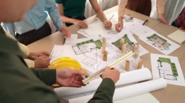 Mimari belge, ölçüm aracı ve ahşap blokların modern ofiste etrafa saçıldığı bir masa üzerinde yapı inşaatı ile ilgili mimar ve güvenlik mühendisi tartışması. Tanımlama.