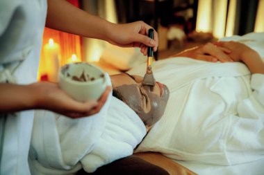 Kaplıca salonunun sakin atmosferi, kadın müşteri sıcak mum ve kömür kömürü yüz kremi masajıyla kendini yenileme zevkine kapılıyor. Yüz bakımı ve güzellik konsepti. Sessiz.