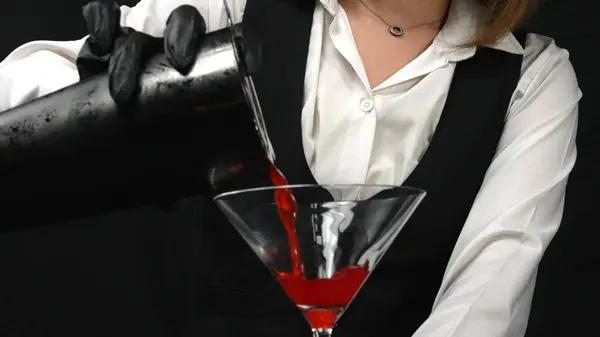 stock image Macrography, witness the artistry of a bartender pouring a vibrant red cocktail in a martini glass, beautifully adorned with a sprig of fresh rosemary against a sleek black background. Comestible.