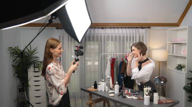 İki kadın nüfuzlu partner sosyal medya veya blog için canlı yayın yapan video klip inceleme derisi çekiyorlar. Kozmetik stüdyosu ışıklandırması olan genç bir kız pazarlama oturumu çevrimiçi yayın yapıyor.