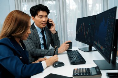 Gülümseyen Asyalı işadamı komisyoncu dinamik borsa veritabanını arıyor. Kadın iş ortağı, iç işyerindeki kar eden uygulama programını karşılaştıran ekranlara işaret ediyor. İnfobahn.