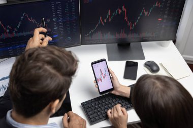 İki iş adamının internet sitesindeki dinamik borsa tartışmalarına odaklanan üst görünüm, modern ofisteki gerçek zamanlı döviz kuru risk verilerindeki bilgisayar ekranlarıyla karşılaştırılıyor. Varsayım.