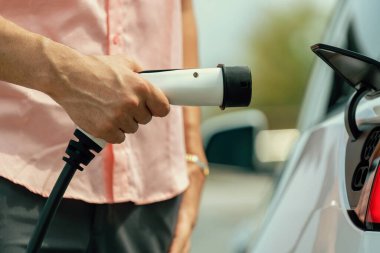 Dışarıdaki şarj istasyonundan EV şarj aletini şarj etmek için elektrikli araca elle tak. Alternatif temiz ve sürdürülebilir enerji kavramına sahip taze gün ışığı ortamı. Kalıcı