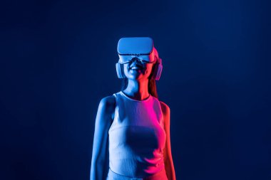Siberpunk neon ışıklı cihazlarla çevrili zeki bir kadın metaevrene bağlı VR kulaklık takıyor, gelecekçi siber uzay teknolojisi. Zarif bir kadın sanal ortamda yaratılmış gibi görünür. Halüsinasyon.