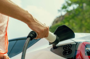 Dışarıdaki şarj istasyonundan EV şarj aletini şarj etmek için elektrikli araca elle tak. Alternatif temiz ve sürdürülebilir enerji kavramına sahip taze gün ışığı ortamı. Kalıcı