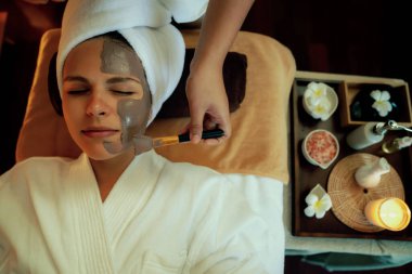 Kaplıca salonunun sakin atmosferi, üst düzey kadın müşteri sıcak mum ışığında kömür kömürü yüz kremi masajıyla kendini yenilemeye çalışıyor. Yüz bakımı ve güzellik konsepti. Sessiz.