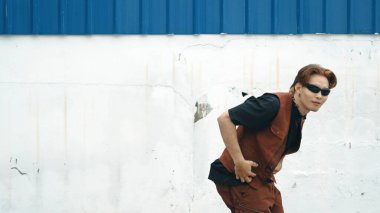 Beyaz arka planda break dans pratiği yapan yakışıklı bir sokak dansçısı. Hip hop tarzı giyinen sporcu, mavi arka planlı bir sokakta müzik eşliğinde ayak sesleri çıkarıyor. Açık hava sporu 2024 hiphop..