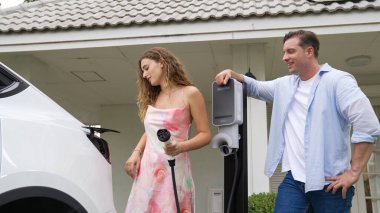 EV şarj istasyonundan çevreci bilinci açık elektrikli araca sahip mutlu ve sevimli bir çift. EV araba teknolojisi gelecekteki sürdürülebilirlik için alternatif ulaşım aracı olarak kullanılıyor. Eşzamanlama