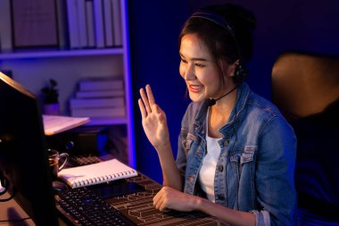 Sunucu kanalı Asyalı etkileyicisi canlı yayında konuşuyor. Sosyal medyada kulaklık takıyor, bilgisayar kaydı yapıyor, dinleyicileri selamlıyor ve Neon Modern Stüdyoları 'nda online olarak koçluk yapıyor. Taktik.