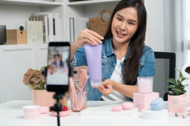 Genç ve güzel Asyalı bir kız nemlendirici vücut kremi ürününü inceleyerek sosyal medyada canlı cilt testi yaparak modern odada en çok satanlarla canlı telefon kaydı yapıyor. Taktik.
