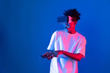 Genç Afrikalı Amerikalı oyuncu sanal gerçeklik dünyasını dijital fütüristik teknolojiye bağlayan mavi neon ışıklı duvarda akıllı telefon oyunu hologramı kullanarak VR kullanıyor. Entrika.
