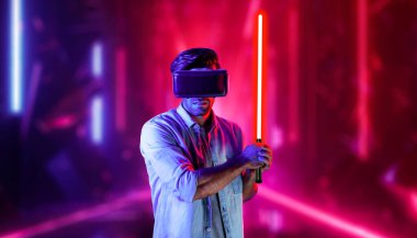 Lazer kılıcı tutan ve VR gözlük takan oyuncu. Beyaz adam, neon şatonun etrafında dikilirken görsel gerçeklik kulaklığı kullanıyor. Yenilik teknolojisi. Sapma.