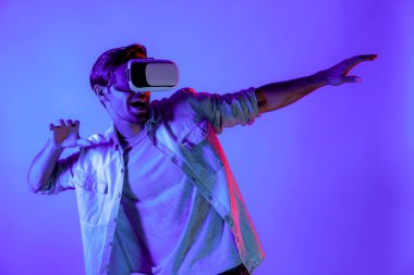Mutlu adam hareketli voleybol hareketini yaparken neon arka planda VR cam kullanıyor. Beyaz tenli genç ve oyuncu gözlük ve yenilik teknolojisi ile spor oyunu oynuyorlar. Sapma.