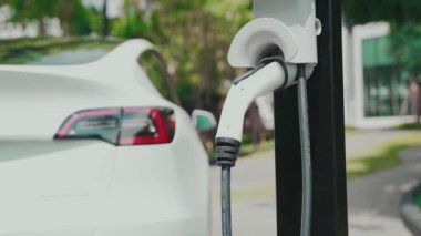 Yavaş çekim EV elektrikli araba yazın yeşil sürdürülebilir şehir bahçesinde şarj oluyor. Kentsel sürdürülebilirlik yaşam tarzı yeşil temiz yeniden şarj edilebilir enerji elektrikli BEV araç iç organları