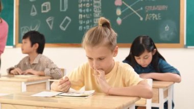 Sınıfta mutlu bir çok kültürlü öğrenci ilkokulda sınıfta sınav yaparken ya da not yazarken beyaz çocuk kameraya gülümsüyor. Eğitim konsepti. Pedagoji.