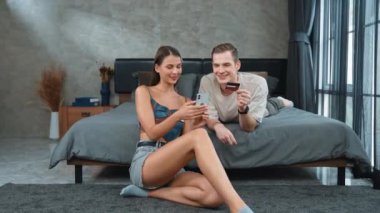 Genç çift, kredi kartıyla ödemek için internet üzerinden ödeme uygulaması ve dijital cüzdan kullanarak yatak odasında oturuyor. Mobil internet üzerinden alışveriş ve modern alımlar. Düzenle