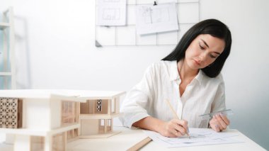 Ofisteki masaya yerleştirilmiş belge ve mimari modelle evin planlarını yazan genç mühendisin yakın plan görüntüsü. Yaratıcı tasarım ve mimar konsepti. Tertemiz..