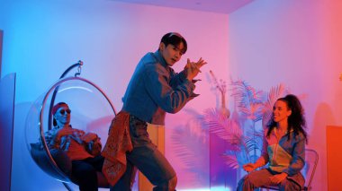 Çok kültürlü bir arkadaş kürsüde otururken Asyalı yetenekli bir dansçı modern müziğe geçiyor. Profesyonel dansçı, hipster takımı tezahürat yaparken ve desteklerken enerjik adımlar atıyor. Mutluluk.