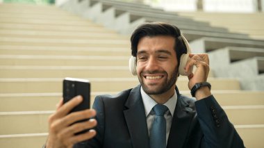 Akıllı telefonlara gülümserken selfie çeken mutlu iş adamı. Profesyonel yöneticinin merdivenlerde takım elbise ve kulaklık takarken görüntüsü. Yaratıcı iş. Sevinçli..