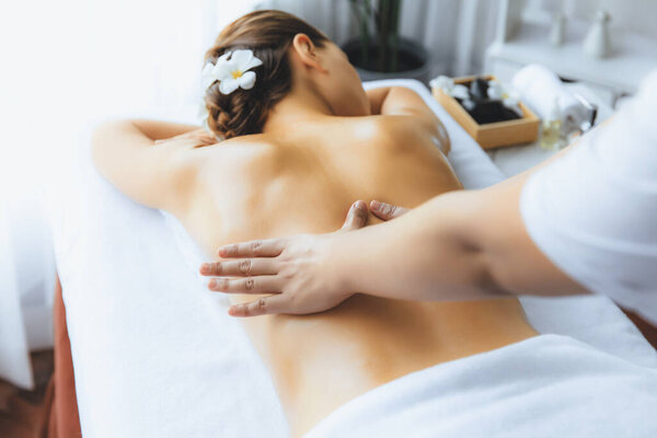 Caucasian woman customer enjoying relaxing anti-stress spa massage and pampering with beauty skin recreation leisure in day light ambient salon spa at luxury resort or hotel. Quiescent