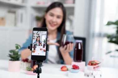Seçici odaklı akıllı telefon ve gülümseyen genç, güzel Asyalı karışık çilek ve kiraz suyu detoksu değerlendirmesi sosyal medyada sağlıklı ürün tanıtımı sunuyor. Taktik.