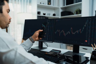 Akıllı telefondan akıllı telefon arayan tüccar işadamı, bilgisayardaki dinamik borsa yatırım ekranını analiz ediyor ve modern merkez ofisteki en kârlı finansal teknoloji pazarına yatırım yapıyor. Tahmin et..