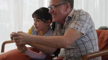 Grandfather and granddaughter together watch interesting entertainment media on TV. Old senior use technology communicate with young generation cross generation gap strengthen family bond. Divergence. clipart