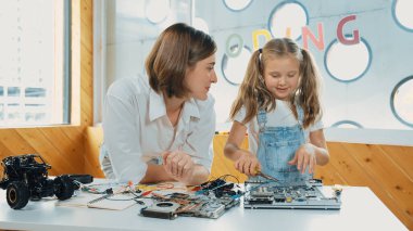 Genç, zeki, beyaz bir öğretmen öğrencilere elektronik kurulun bir parçasını öğretiyor. Uzman kız dijital elektrikli aletleri öğreniyor ve cips ve kablolarla ana kartı tamir ediyor. Etkinlik.