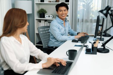 Gülümseyen Asyalı bir adam, yan görüntüdeki modern ofis çalışma masasında veri tabanını ararken günlük dizüstü bilgisayarla pazarlama raporu projesini planlarken kadın meslektaşıyla konuşuyor. İnfobahn.