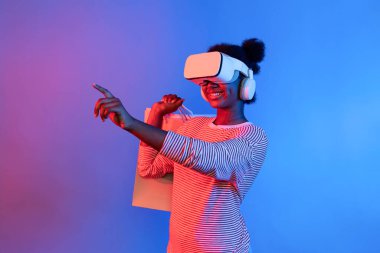 Canlı dijital fütüristik teknoloji meta metasında hologram uygulaması güzellik bezi ürünü üzerinde alışveriş poşeti tutarken İnternet üzerinden alışveriş yapan genç Afrikalıların keyfini çıkarın. Entrika.