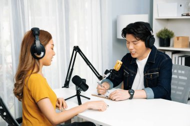 Gülümseyen radyo etkili sunucusu kulaklık takıyor kadın konuşmacı ile röportaj yapıyor sosyal medya internet sitesinden dinleyicilere bilgi paylaşıyor stüdyo kaydında sabah canlı yayın kanalı. İnfobahn.