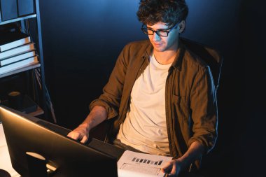 Genç işadamı, Neon Light Modern Ofis 'teki yeni proje surround çalışma masası için kağıt üzerinde tasarım düşünüyor. E-posta ile hediye göndermeden önce not defterine yeni bir iş düşünüyorum. Toplayıcı.