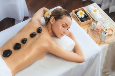 Lüks tatil köyündeki kaplıcalarda sıcak taş masajı. Gün ışığı sükunet ortamında, mutlu kadın müşteri bazalt taş masajından zevk alıyor. Rahatlatıcı bir sıcaklıkla vücudun üzerinde süzülüyor. Sessiz.