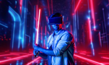 Lazer kılıcı tutan ve VR gözlük takan oyuncu. Beyaz adam, neon şatonun etrafında dikilirken görsel gerçeklik kulaklığı kullanıyor. Yenilik teknolojisi. Sapma.