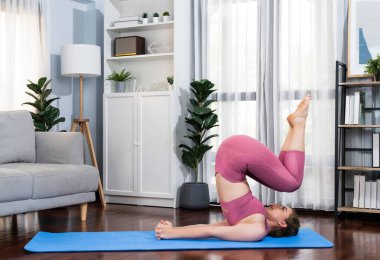 Spor kıyafetleri içinde esnek ve becerikli bir kadın evde egzersiz paspası üzerinde meditasyon pozisyonunda yoga yapıyor. Huzurlu ve huzurlu bir yoga yaşam tarzı..