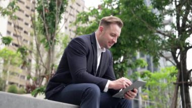 Tablet kalemle yazarken parkta oturan işadamının yan görüntüsü. Akıllı proje yöneticisinin finansal planı düşünürken veri analizine baktığı düşük açılı kamera. Urbane