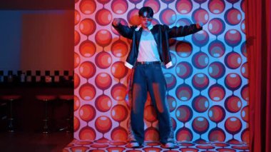 Asyalı break dansçı serbest stile geçiyor ve balon arka planlı kameraya bakıyor. Profesyonel hippi gündelik kıyafet giyer ve gözlük takar. Mutluluk.