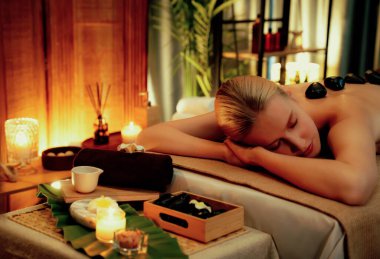 Lüks tatil köyündeki kaplıcalarda sıcak taş masajı, sıcak mum ışığı, spa bazalt taşı masajının keyfini çıkaran mutlu kadın müşteriler, rahatlatıcı bir sıcaklıkla vücudun üzerinde süzülüyorlar. Sessiz.