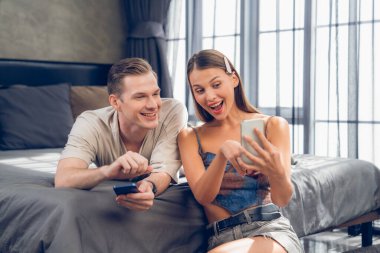 Genç çift, kredi kartıyla ödemek için internet üzerinden ödeme uygulaması ve dijital cüzdan kullanarak yatak odasında oturuyor. Mobil internet üzerinden alışveriş ve modern alımlar. Açılıyor