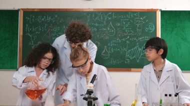 Kafkasyalı zeki öğretmen, meraklı öğrencilerin laboratuardaki deney kabına renkli sıvı dökmesini destekler. Yaratıcı çocuklar deney yapmaya ve biyokimyasal örnekleri incelemeye konsantre olurlar. Pedagoji.