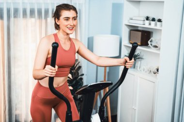Spor ve atletik bir kadın, evdeki fiziğe ve sağlıklı spor yaşam tarzına uygun vücut egzersizi sırasında eliptik koşu makinesiyle koşuyor. Gaiety evde egzersiz eğitimi.