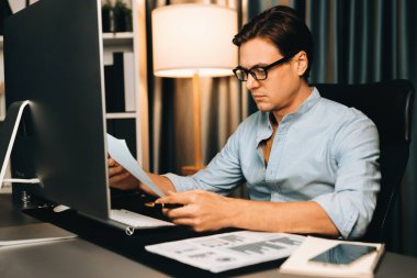 Akıllı iş adamı iş paragrafı dinamik pazarlama analizi planını analiz ediyor. Kağıt kağıtları ve bilgisayar monitörü raporlarını gece evdeki belge verileriyle karşılaştırmak için hazırlıyor. Bireysel.