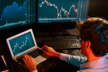 Dizüstü bilgisayarda araştırma yapan genç yatırımcı hisse senedi tüccarı, güncel pazar grafiğinin dinamik döviz kuru ekranlarıyla gerçek zamanlı olarak neon ışığı modern ofisinde finansal verileri analiz ediyor. Toplayıcı.