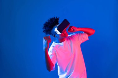 VR giyen Afro-Amerikan boksör boksör boksör, boksör yumruğu kamerasıyla fütüristik teknoloji sanal gerçeklik metaevren dövüş kutusunu birbirine bağlayan izole edilmiş pembe ışıklı duvar pozu veriyor. Entrika.